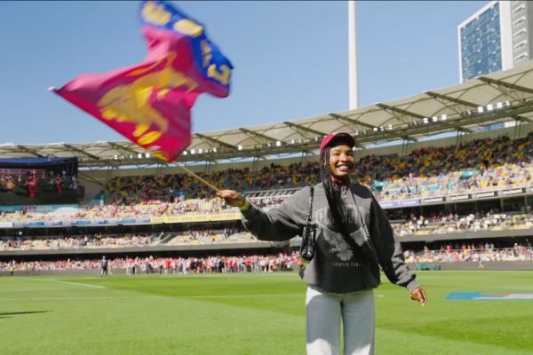 A woman waving a Lions AFL flag while standing on the field at the Gabba.